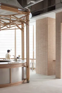 A restaurant interior with a wooden theme, featuring a metal countertop, sink, and coffee maker, with two people in the scene