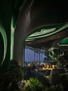 A cozy restaurant dining area with a large green wall, multiple chairs, and dining tables with wine glasses and bottles