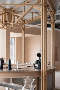 A rustic workspace or communal gathering area with a large wooden dining table and chairs, and a smaller table in the background, with cups on the main table suggesting recent use