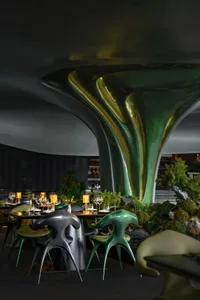 Modern dining space with chairs, wine glasses, and vases on marble and metal tables, warm and inviting ambiance with natural and artificial lighting