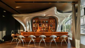 A modern bar area with a counter and chairs, featuring bottles and a welcoming atmosphere
