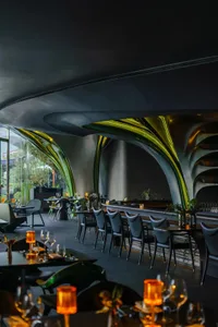 A cozy restaurant with a long dining table, chairs, and potted plants, creating a warm and inviting atmosphere for socializing and dining