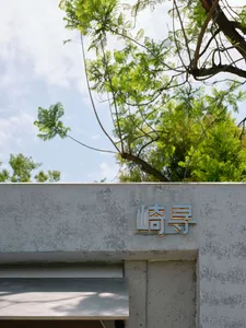 Gray concrete building with a metal sign and a modern appearance, surrounded by trees in an urban environment