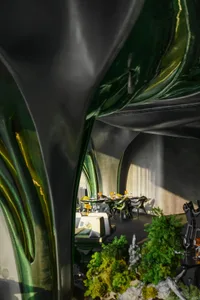 Casual restaurant dining area with multiple tables, chairs, and potted plants, with backpacks on some chairs