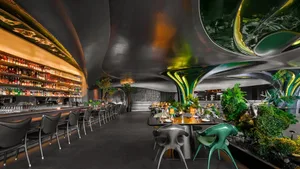 A warm and inviting restaurant interior with multiple dining tables, potted plants, and comfortable seating for guests