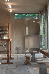 A modern bathroom with concrete walls, a sink area, a mirror, and a toilet, featuring two stools and a clean, contemporary design