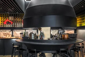Industrial kitchen with a black countertop, stools, and dining chairs, featuring various kitchen items and a comfortable dining area