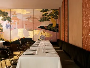 A beautifully decorated dining area with a long table, chairs, and various table settings, surrounded by painted birds in a sophisticated restaurant setting