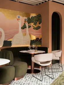 Elegant cafe interior with a dining table, chairs, and swans on the wall, surrounded by pink walls and wine glasses