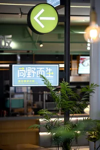 A well-lit Asian restaurant with a green sign featuring Chinese characters, surrounded by potted plants and two TVs on the wall
