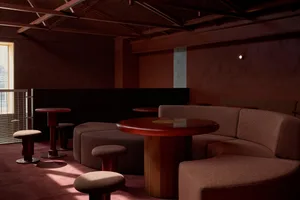 Cozy restaurant interior with red walls, wooden tables and chairs, and a modern seating area with couches