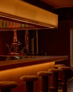 A dimly lit bar with a modern design, featuring a large counter with stools and bottles on display, in a warm atmosphere with brown and orange tones