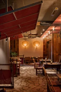Warm and inviting restaurant interior with wooden floors, red walls, and ceiling lights, featuring dining tables, chairs, and potted plants