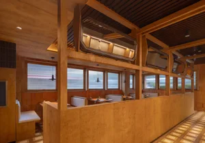 Warm and inviting restaurant interior with wooden walls and ceiling, multiple dining tables and chairs, and natural light from windows