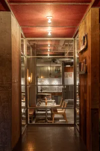 透過玻璃門可見的溫馨餐廳用餐區，配有桌椅與酒瓶