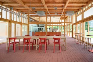 Spacious restaurant interior with a large wooden dining table surrounded by red chairs, creating an inviting atmosphere