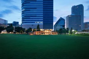 一座擁有眾多窗戶與醒目立面的現代辦公大樓，位於夜晚的城市中，周圍環繞樹木