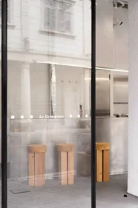 An inviting ice cream shop with wooden stools, a display case, and a refrigerator, set against a neutral background