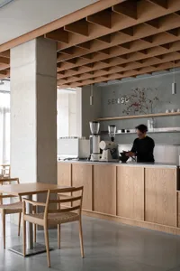 A casual coffee shop interior with wooden floors and walls, featuring chairs, dining tables, and a counter with baristas preparing drinks