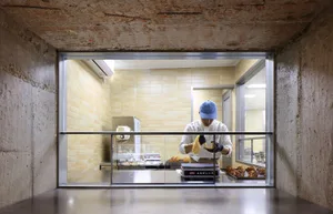 一名戴藍帽男子在專業廚房環境中於料理台上準備食物，周圍有多個甜甜圈與碗盤