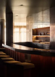 A modern bar area with a large wooden counter featuring a marble top, wine glasses, and bottles, set in a sophisticated and inviting atmosphere