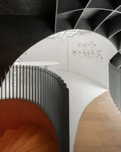 A spiral staircase with a wooden railing in a white-walled space