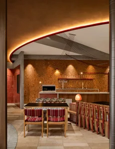 Warm and inviting kitchen and dining area with wooden floors and walls, featuring a dining table and chairs, couches, and decorative bottles