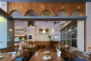 Dimly lit restaurant interior with wooden floors, tables, and chairs, surrounded by potted plants