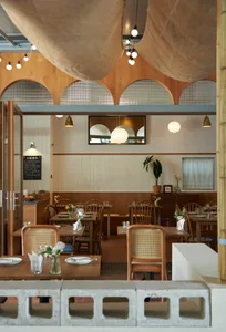 Warm restaurant interior with wooden tables, chairs, and flooring, surrounded by potted plants and a blend of traditional and modern elements