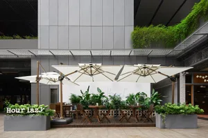 A restaurant patio with tables, chairs, and umbrellas surrounded by potted plants, creating a welcoming atmosphere for outdoor dining