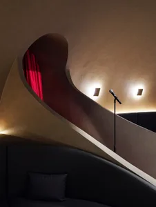 Elegant home theater with a spiral wooden staircase, red curtain, and a microphone on a stage
