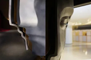 A close-up of a modern metal art piece with a wider view of the surrounding area in the background