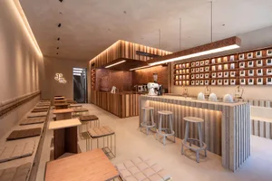 A cozy cafe with a bar area, stools, and dining tables, featuring comfortable seating and scattered cups and bottles