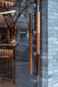 Interior view of a building with a glass door, wooden panels, and chairs in a public or shared living area, with a car visible in the background