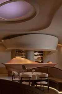 Modern restaurant interior with a curved wall, a dining table, and chairs, featuring bottles on the countertop