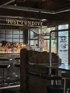 休閒酒吧場景，設有金屬吧台與座椅，周圍環繞酒瓶與輕鬆氛圍