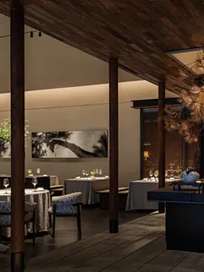 A well-designed restaurant interior with wooden floors and walls, featuring dining tables, chairs, wine glasses, and potted plants