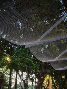 A modern building with a mesh-like metal facade and trees in front, creating a striking visual contrast