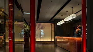 Modern hotel lobby with a red pillar, wood, and glass elements, two potted plants, and inviting atmosphere