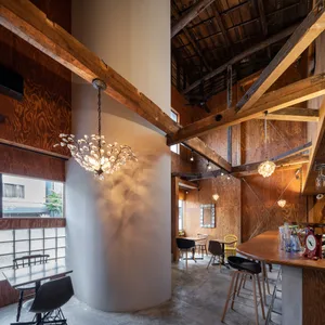 A modern rustic bar area with wooden floors and walls, featuring chairs, dining tables, and a large hanging light, creating a cozy atmosphere