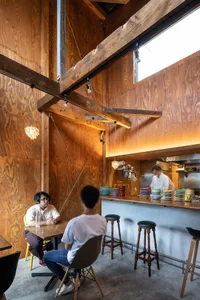 Dimly lit restaurant bar with wooden decor, patrons seated at tables with bowls and drinks, creating a warm and inviting atmosphere