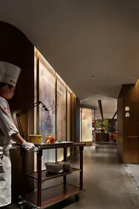 A restaurant dining area with wooden tables, chairs, and a person standing near the left side, set up for guests to enjoy their meals in a cozy environment