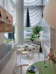 A cozy restaurant dining area with wooden tables, chairs, and wine glasses, creating an inviting atmosphere for socializing and meals