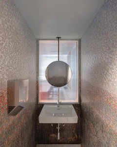 Bathroom with a white sink, circular mirror, and tiled wall, featuring natural light from a window