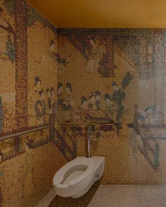 A modern bathroom with a white toilet in front of a yellow wall featuring an artistic design with people and other elements