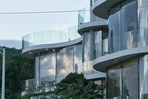 Two modern buildings with glass facades, one curved and one rectangular, surrounded by trees and urban atmosphere