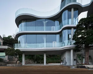 A modern building with a glass exterior, featuring a minimalist and functional design with a focus on open spaces and natural light, set against a backdrop of a tree and a subtle blend of rendered and photographic elements