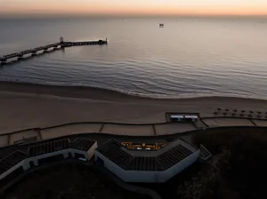 A beachside resort with a large white building and multiple levels, surrounded by umbrellas and situated near the ocean