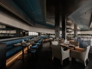 A modern restaurant interior with a large dining area featuring wooden tables and chairs, wine glasses, and an inviting atmosphere