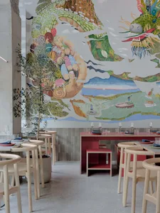 A warm and inviting restaurant interior with a large mural, tables, chairs, wine glasses, and various dishes